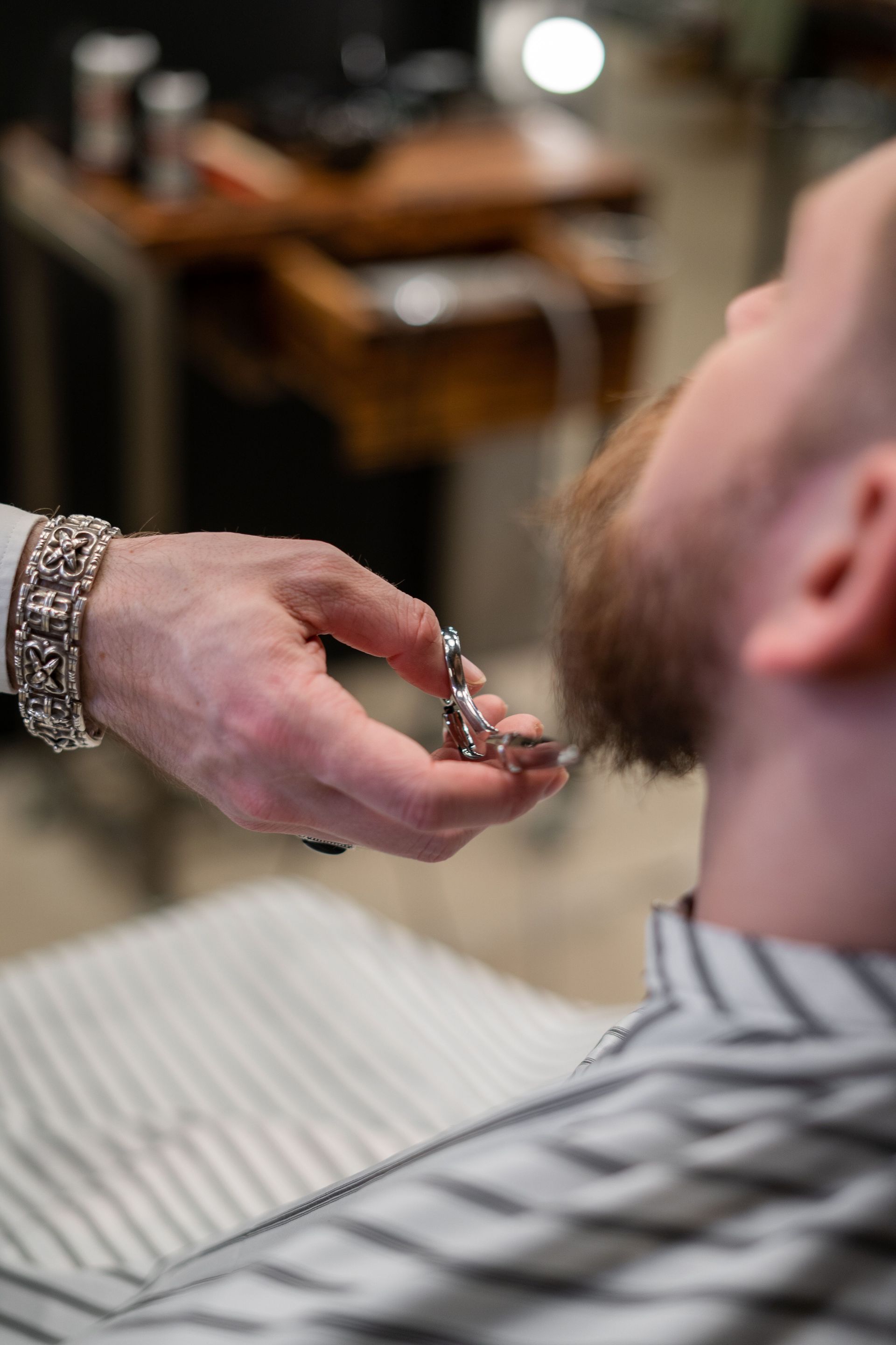 A barber expertly trims a client's beard in a stylish salon setting. Close-up shot.